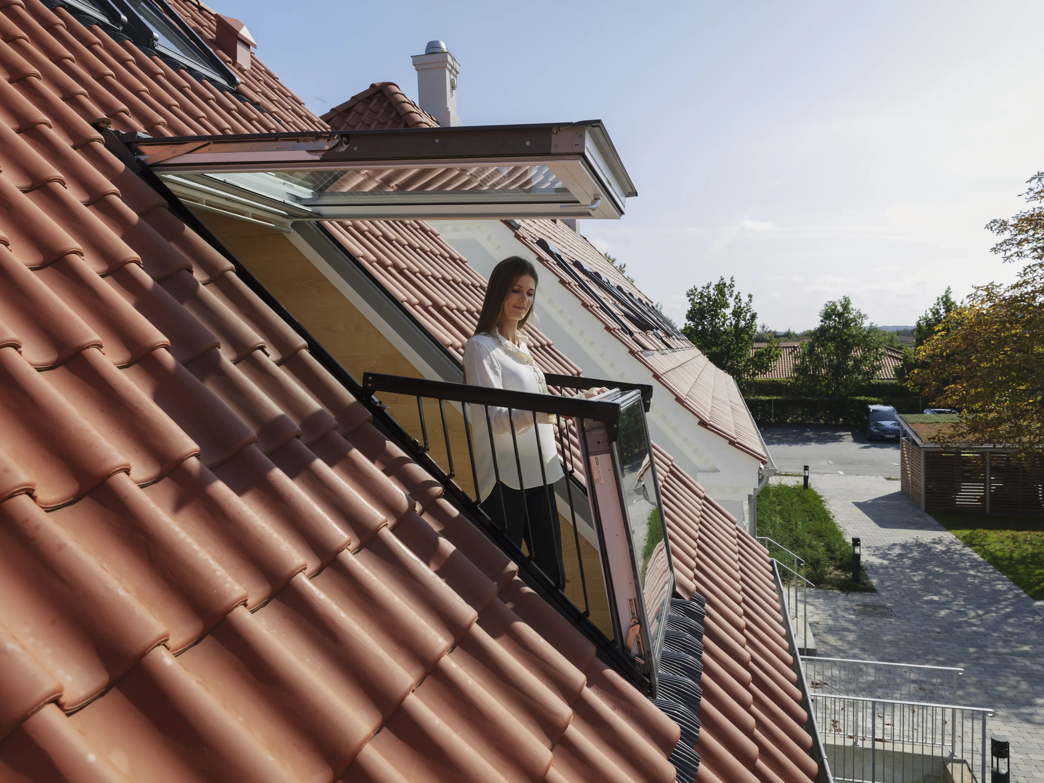 Frau auf geöffnetem Velux CABRIO Balkon-Dachfenster – Blick über Ziegeldach und Garten